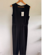 Black jumpsuit on a hanger against a white wall