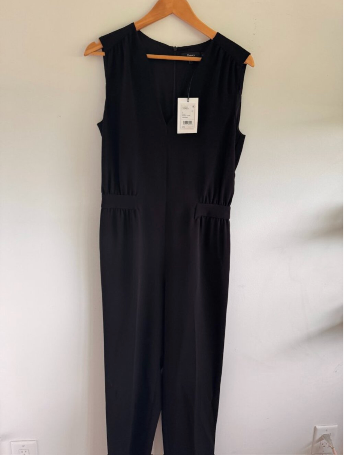 Black jumpsuit on a hanger against a white wall