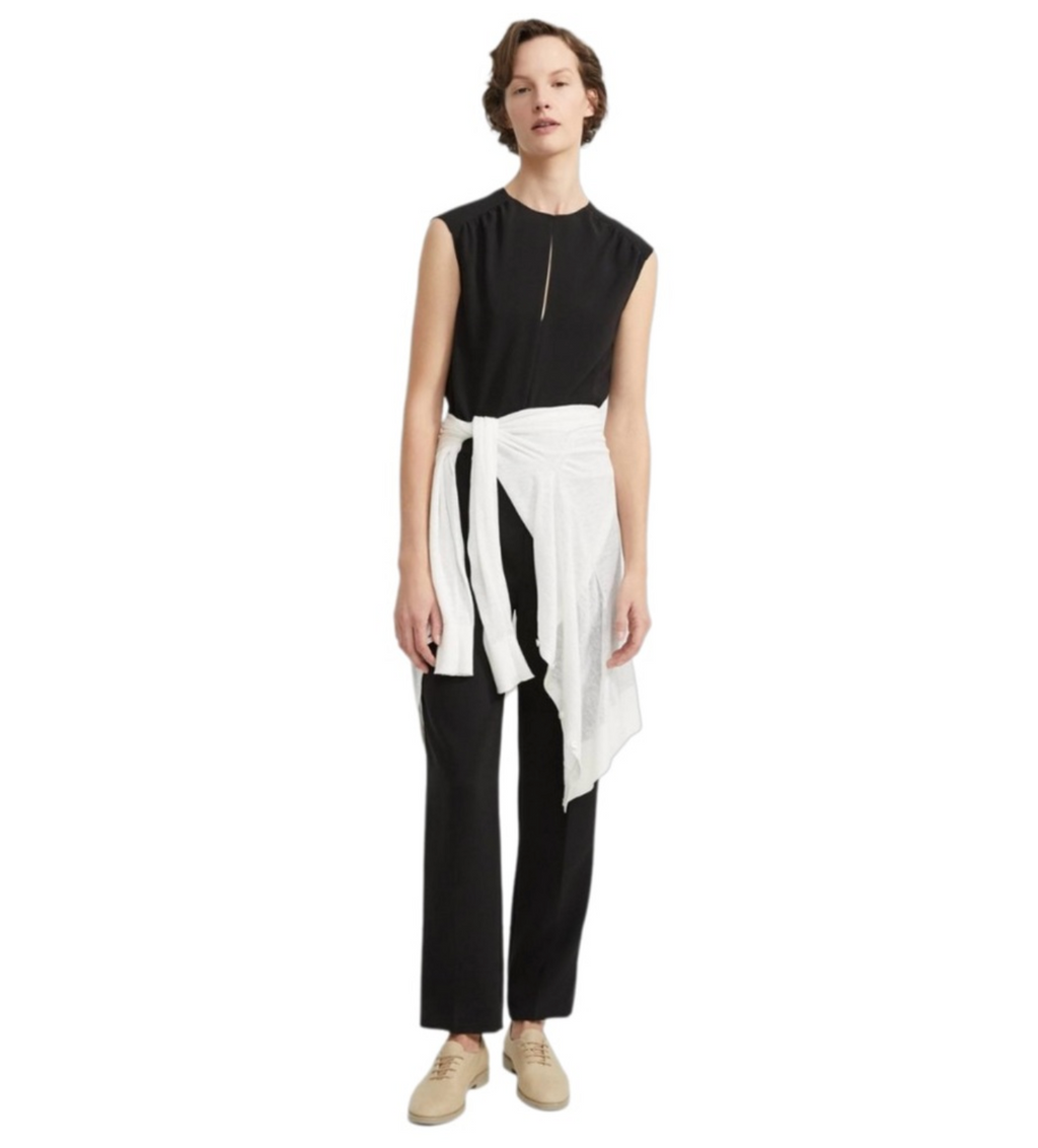 Person wearing a black sleeveless Theory  jumpsuit with a white sweater tied at the waist on a white background