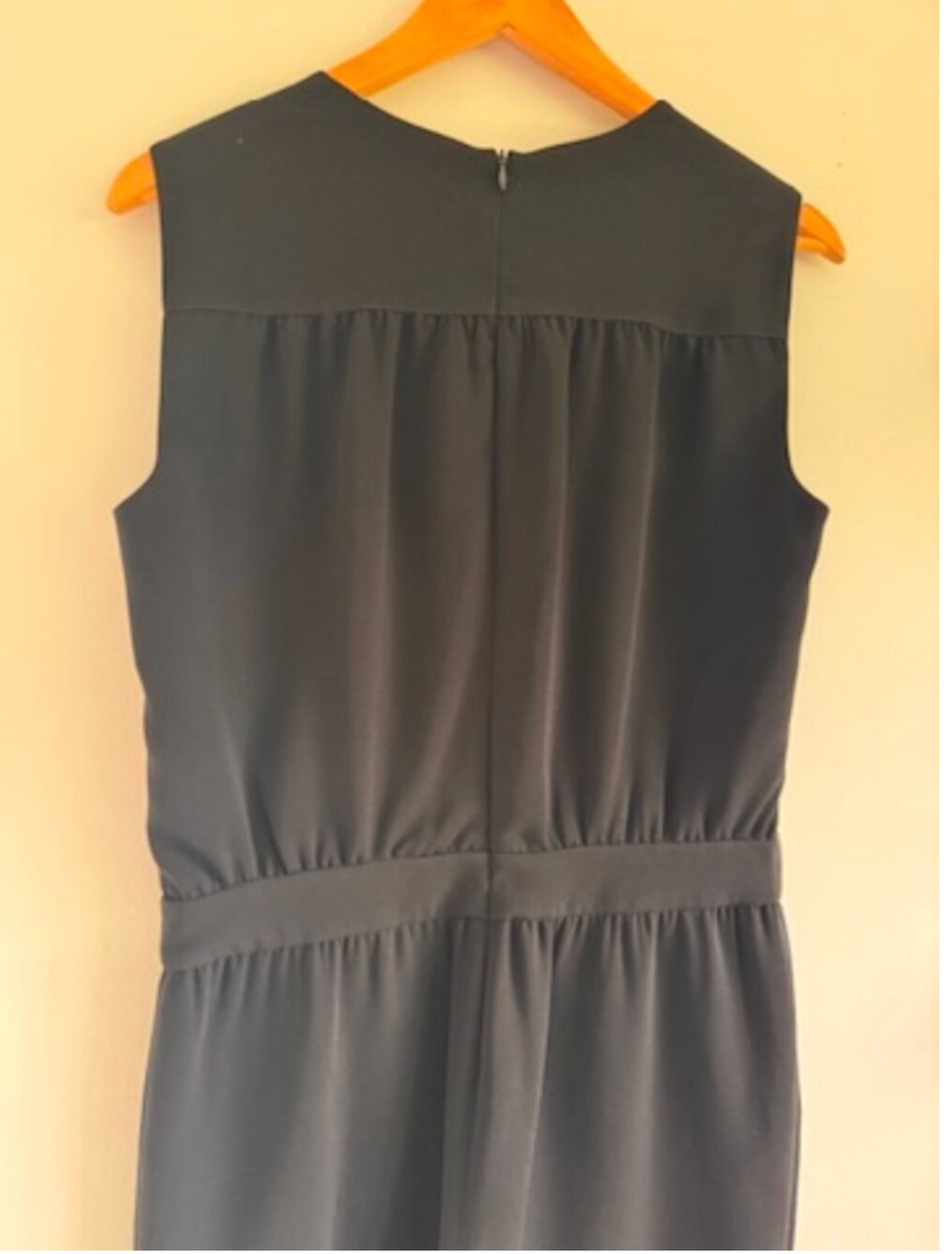 Gray sleeveless dress on a wooden hanger against a beige wall