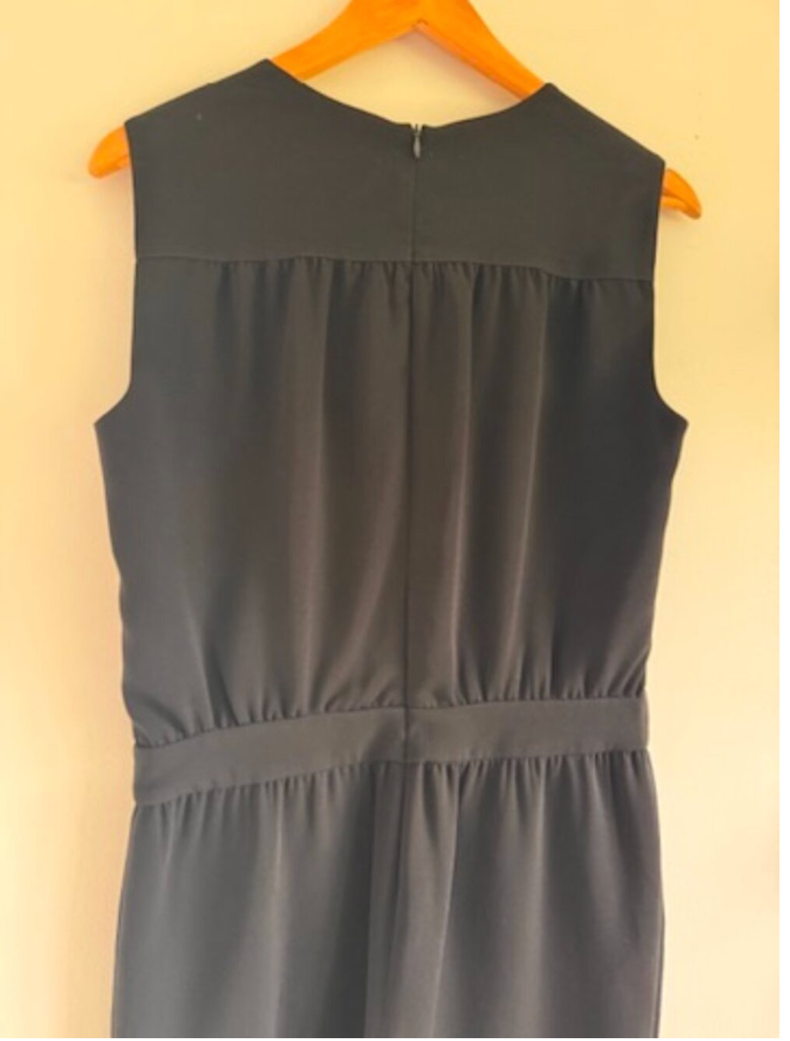 Gray sleeveless dress on a wooden hanger against a beige wall
