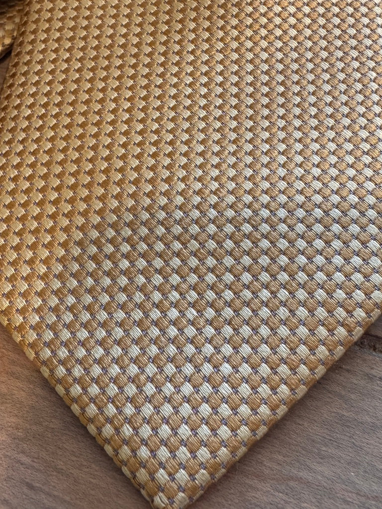A close-up of a necktie a textured basketweave pattern in natural tan and beige, shown on a dark wood surface.