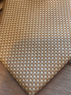 A close-up of a necktie a textured basketweave pattern in natural tan and beige, shown on a dark wood surface.