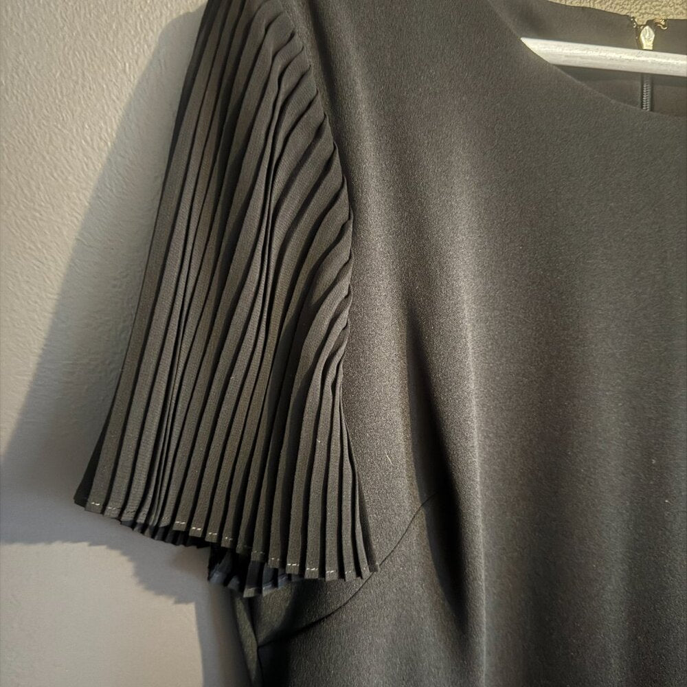 Black dress with pleated detail on a hanger against a white wall