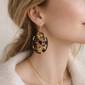 Close-up of a person wearing gold earrings and a necklace against a neutral background