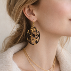 Close-up of a person wearing gold earrings and a necklace against a neutral background