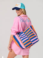 Woman wearing a pink shirt and colorful striped bag on a light gray background