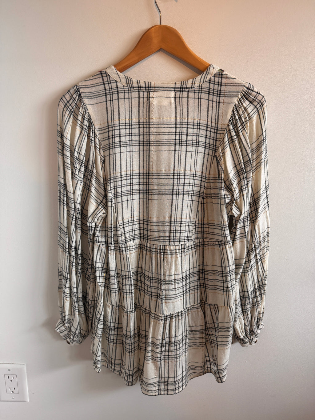 Plaid shirt on a hanger against a plain wall