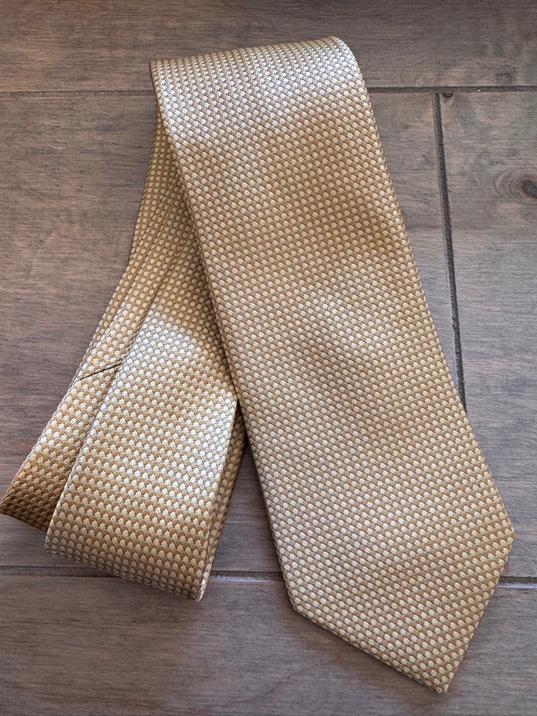 A yellow and beige patterned silk necktie with a small geometric lattice design, laid flat on a dark wood background.