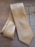 A yellow and beige patterned silk necktie with a small geometric lattice design, laid flat on a dark wood background.