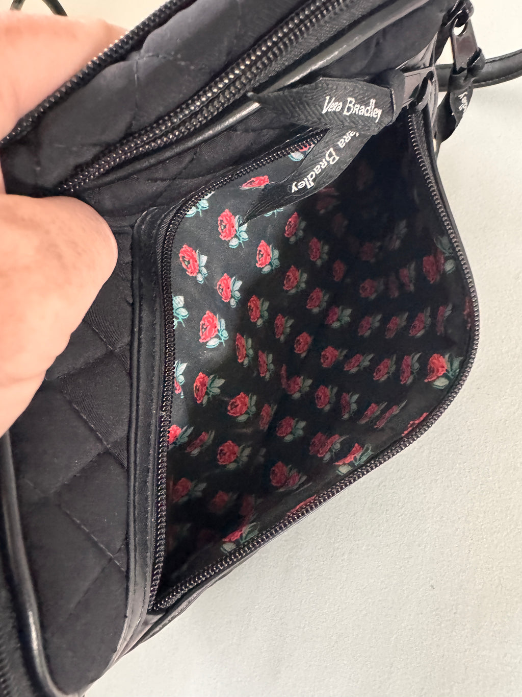 Black quilted bag with floral lining held by a hand against a neutral background