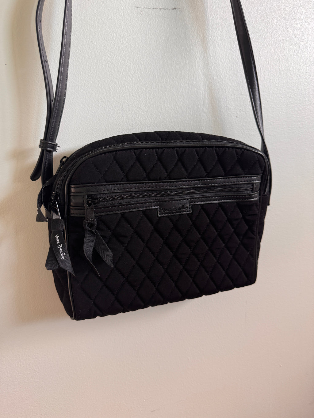 Black quilted handbag with a strap on a light beige background