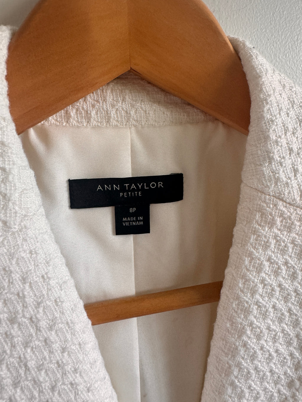 White garment with a brand label on a wooden hanger against a white background