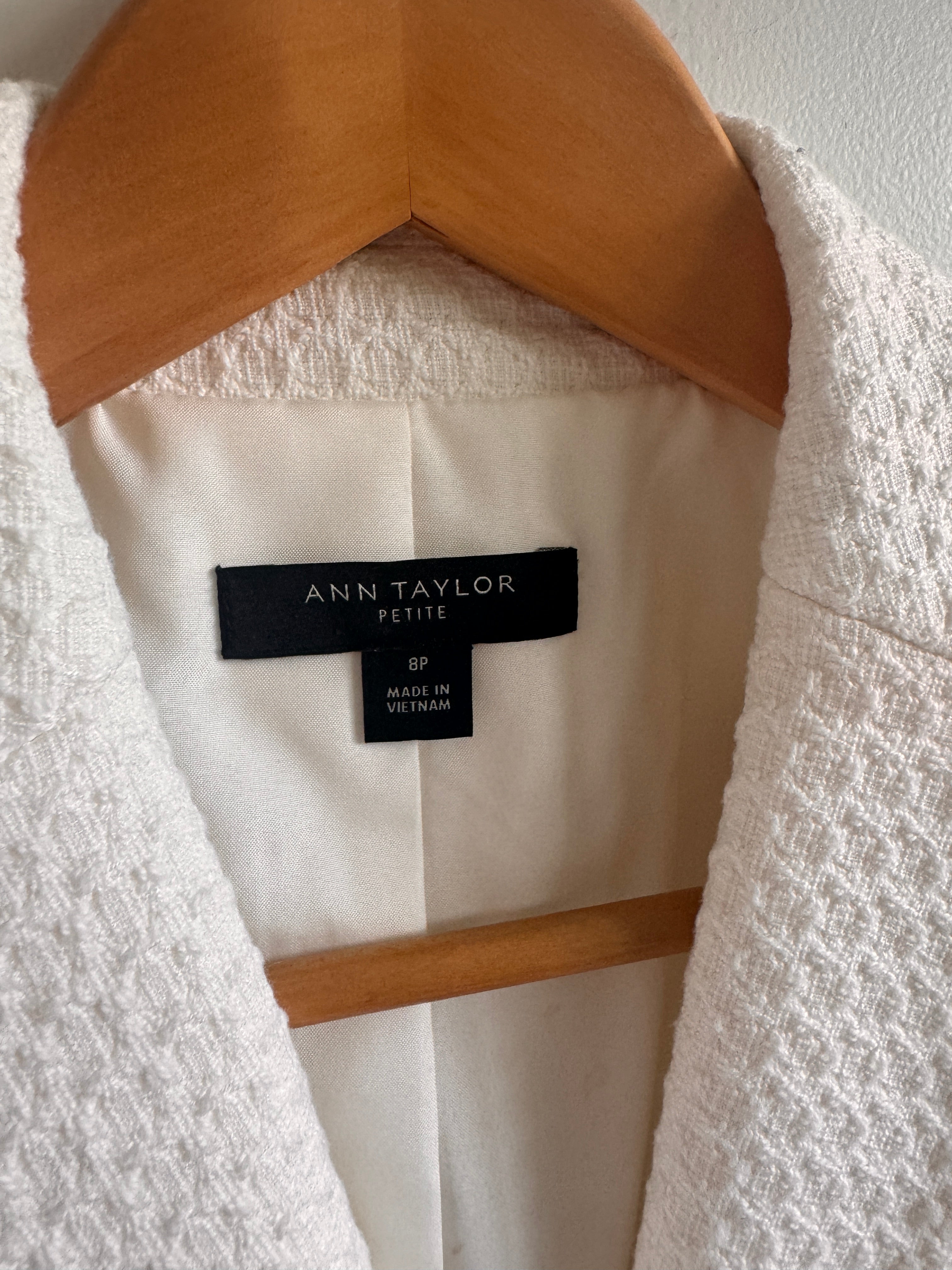 White garment with a brand label on a wooden hanger against a white background