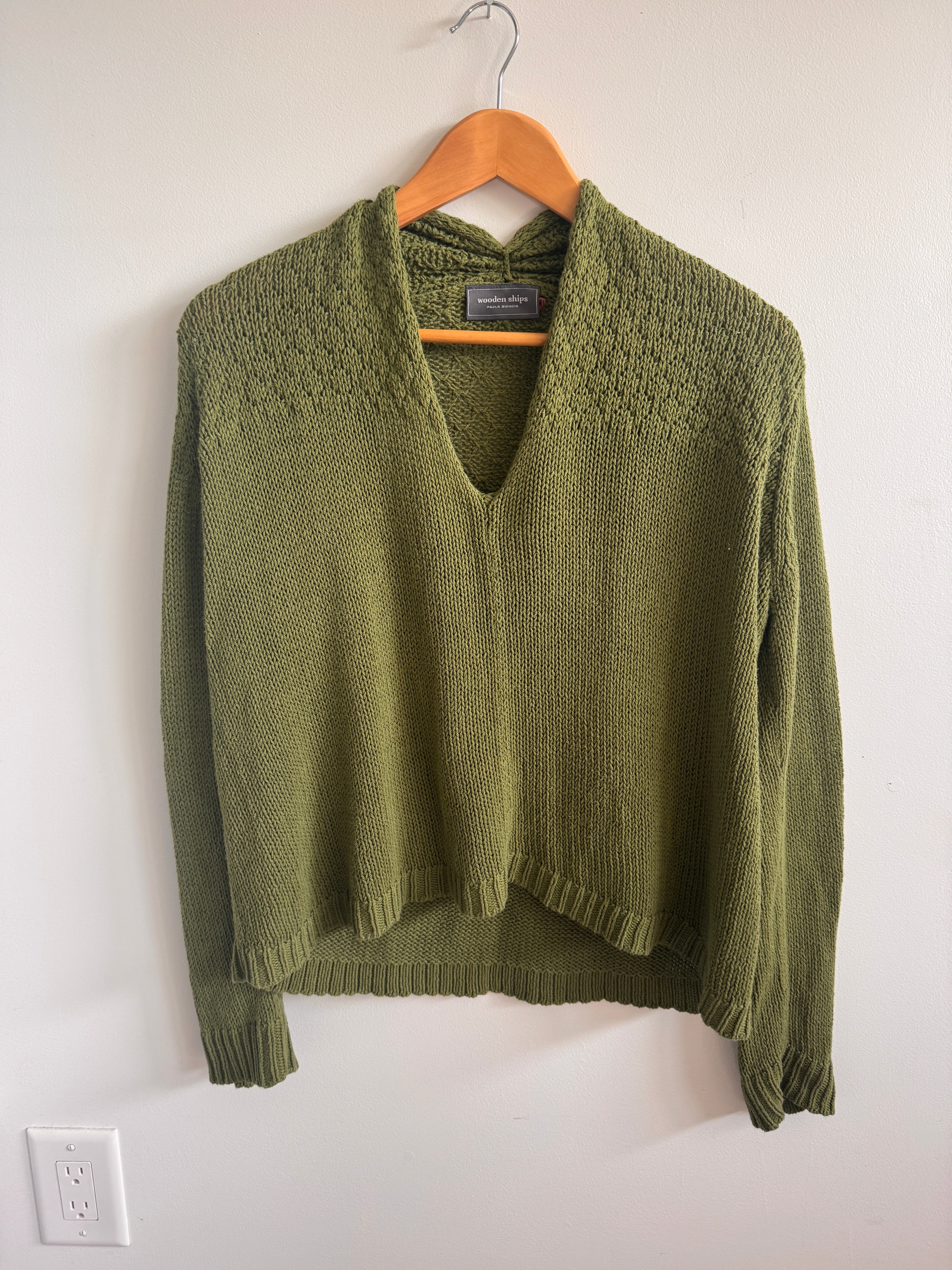 Green sweater on a hanger against a white background