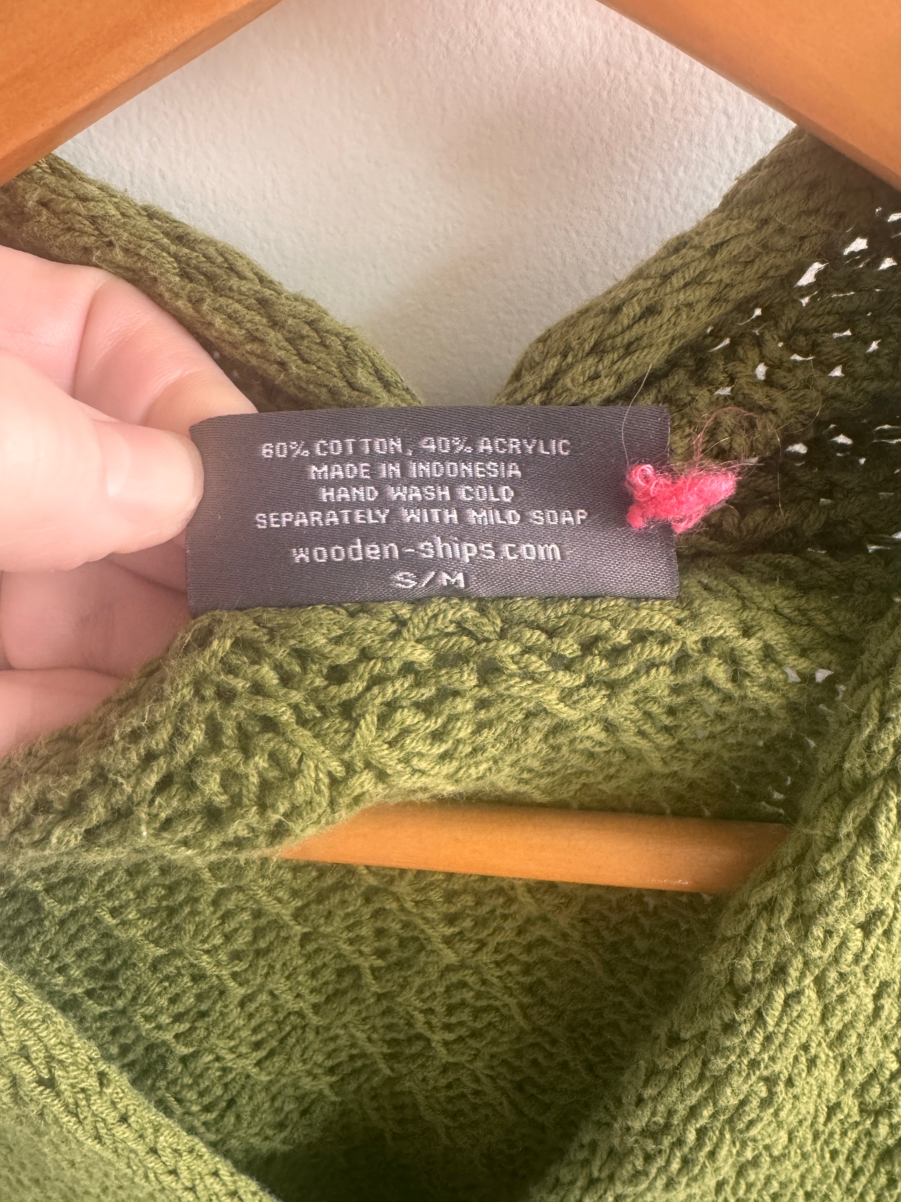 Green knitted garment with a label held by a hand