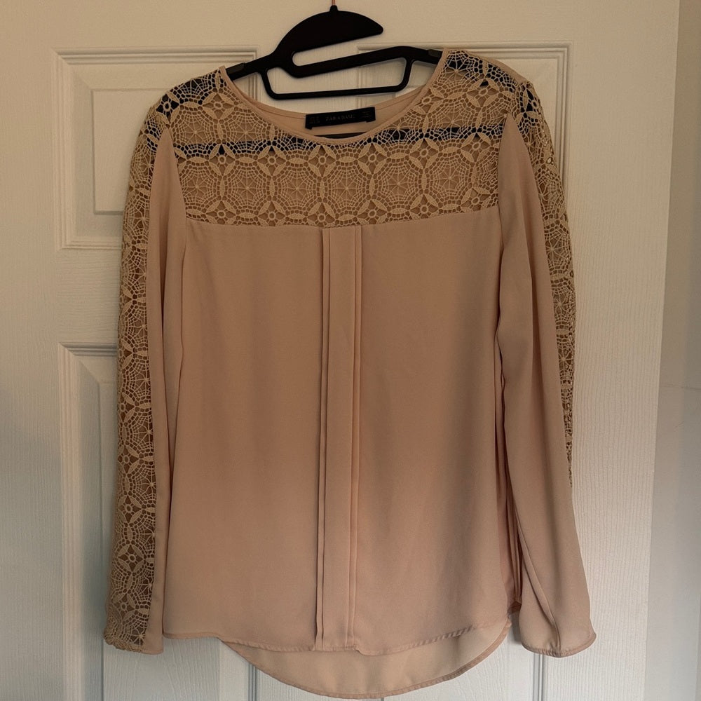 Beige long-sleeve top with lace details on a hanger against a white door.