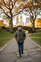 Young boy in olive puffer jacket with pageboy hat walking in Central Park