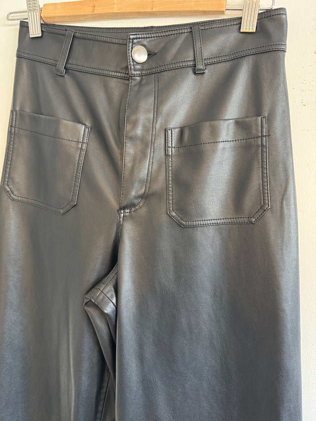 Close-up of a black leather pants with two pockets on a wooden stand.