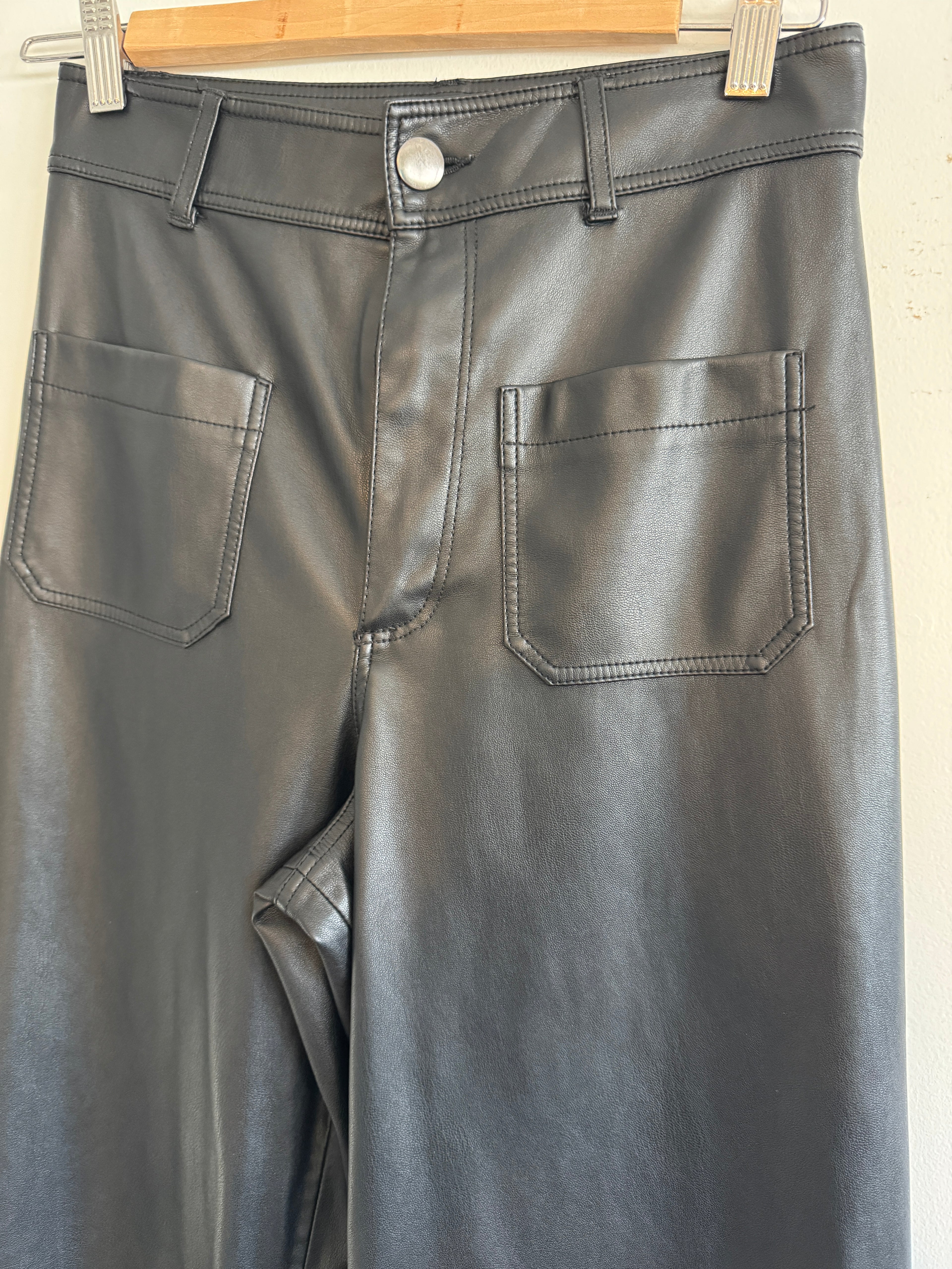 Close-up of a black leather pants with two pockets on a wooden stand.